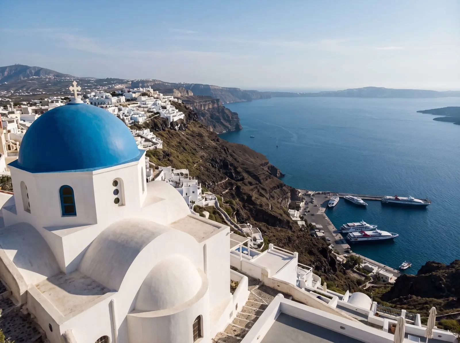 Blue-domed church above the Santorini caldera, with ferries docked at Athinios port below